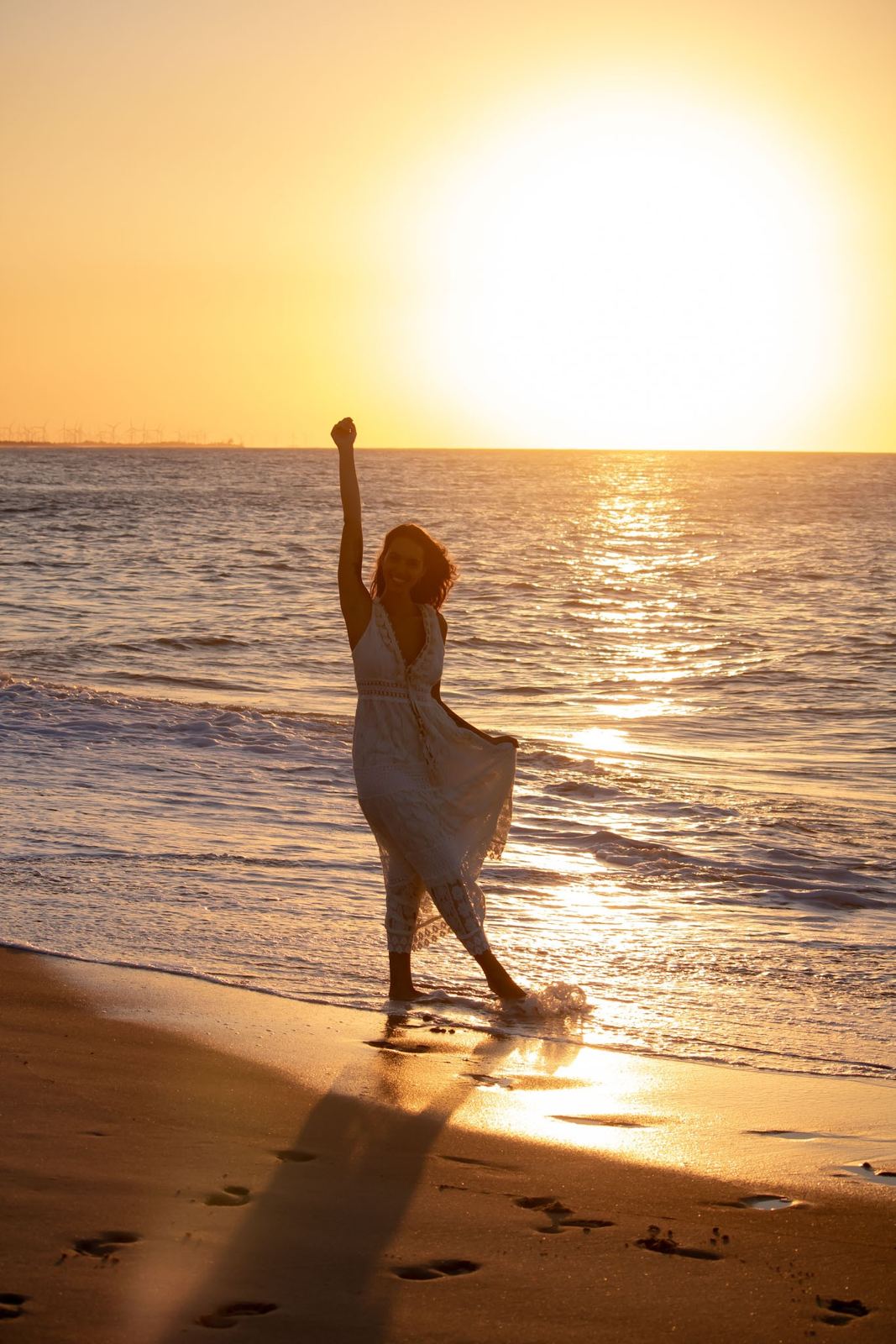 Gabi na praia ao pôr do sol, de braço erguido